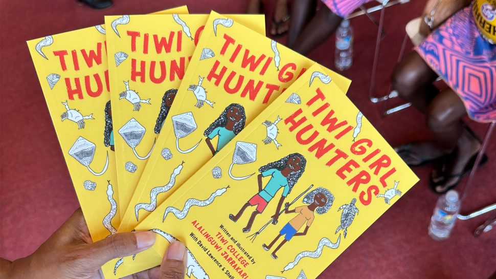 Four copies of a book titled Tiwi Hunters. It has a yellow cover and illustration of young female hunters and animals. 