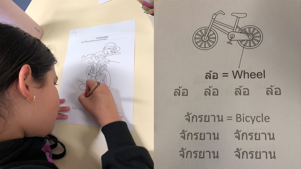 On left - A girl filling in an activity sheet that has a drawing of a cyclist on it. On right - An image of a bicycle with words written in Thai beneath it.