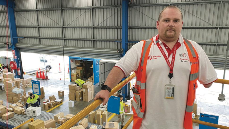 An Australia Post employee with a physical disability is standing in a parcel facility.